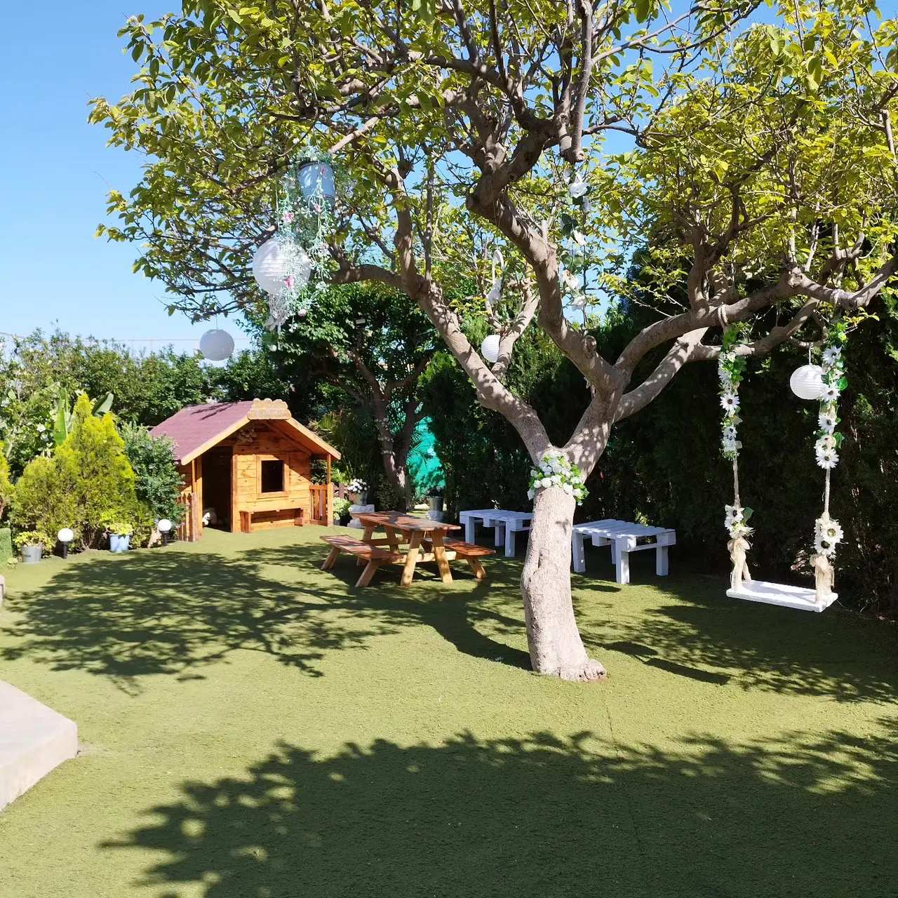 Jardín de Villa Meli con casita de madera, mesa de pícnic y árbol decorado con farolillos