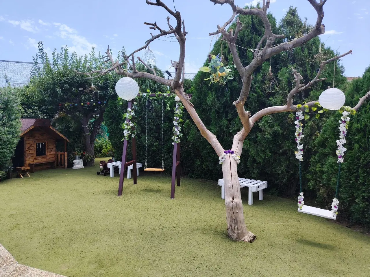 Columpios de madera y árbol decorado con flores y farolillos en el jardín de Villa Meli