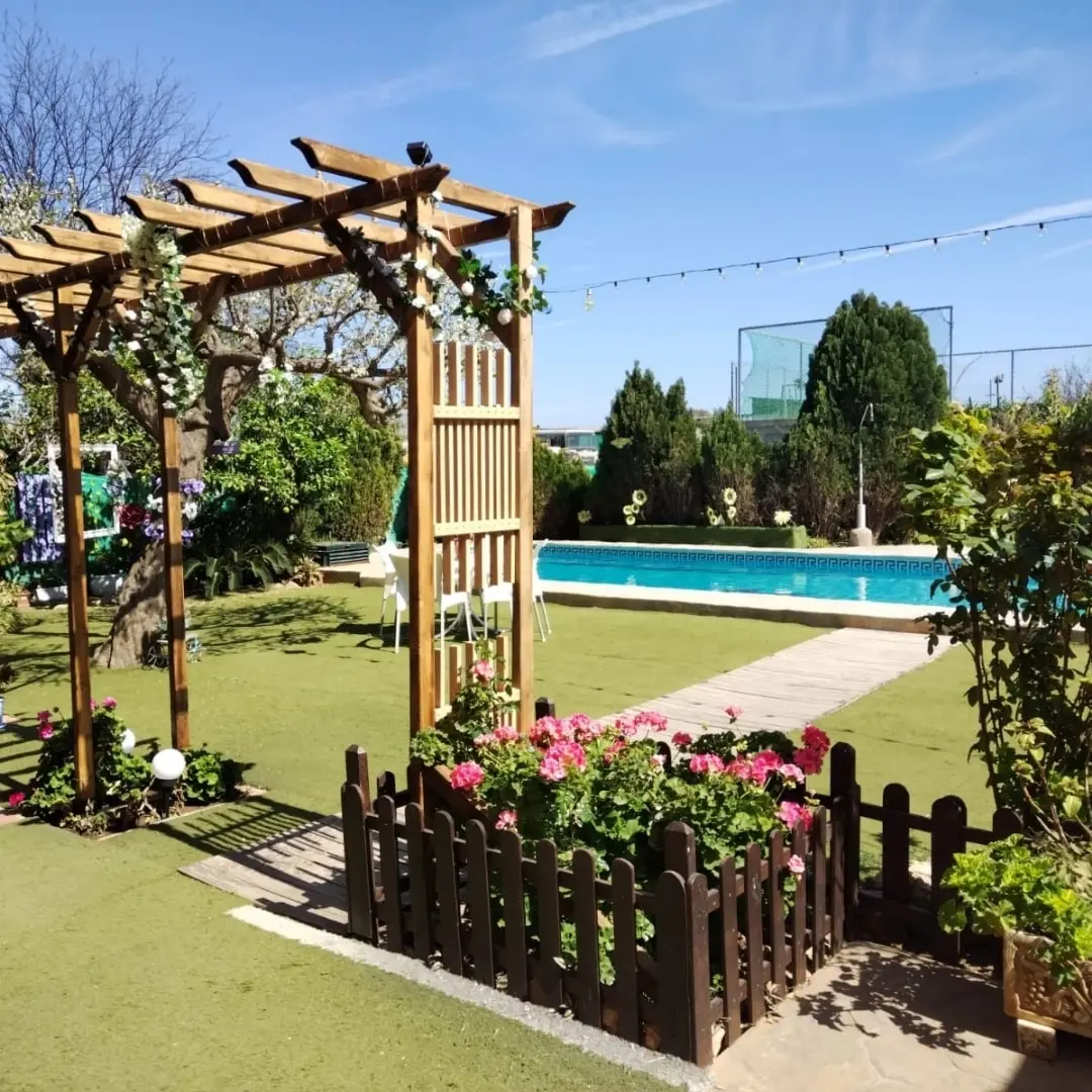 Pérgola de madera con trepadoras y jardinera de geranios, con la piscina de Villa Meli al fondo