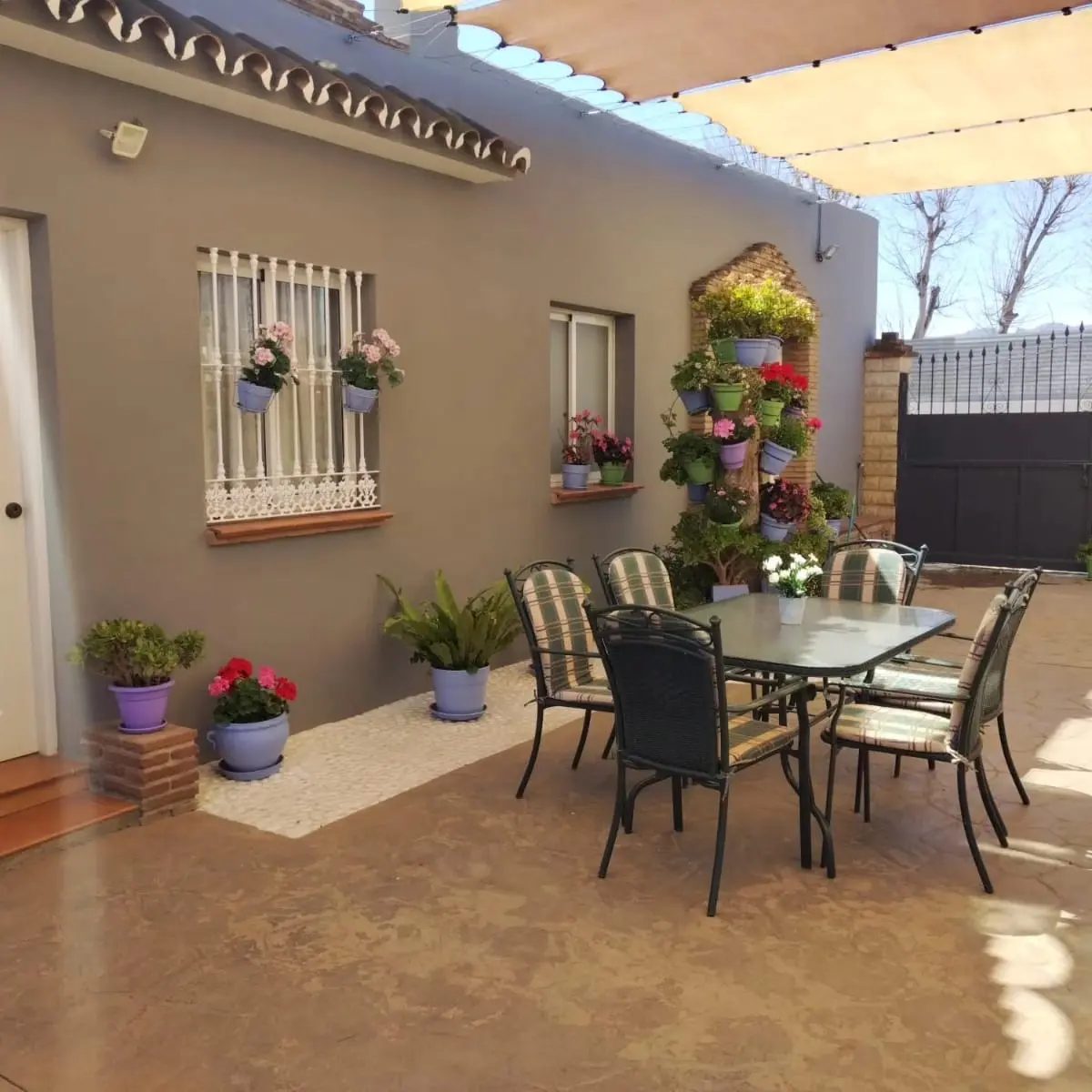 Porche de Villa Meli con macetas de geranios, mesa y sillas junto a la fachada